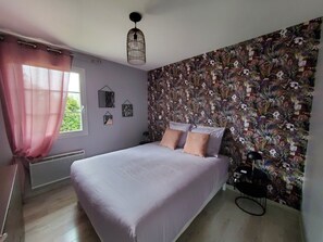 Une chambre à coucher avec un lit, une fenêtre avec des rideaux, un papier peint à motifs floraux et un luminaire au plafond.
