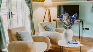 A living room with two beige armchairs, a white coffee table, a floor lamp, and a vase with blue flowers. - Four Season's Splendor: Artist's Nest beside Walled Garden on Seaside Estate (Portpatrick)