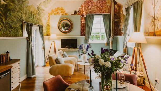 A cozy living room with a fireplace, comfortable seating, a television, and a dining area with a table set for two. - Four Season's Splendor: Artist's Nest beside Walled Garden on Seaside Estate (Portpatrick)