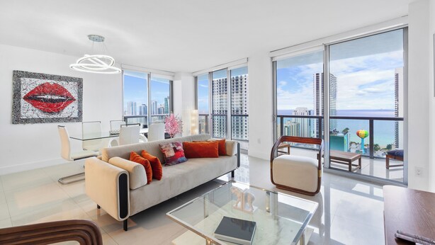 Uma sala de estar ampla, com um sofá moderno, uma mesa de centro de vidro e vista para o horizonte da cidade através de grandes janelas.