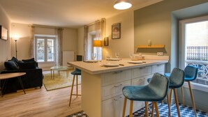 A modern kitchen with a central island, bar stools, and a dining area with a sofa and table. - Appartement T3 de 60 m2 - Centre Historique (Sarlat-la-Canéda)