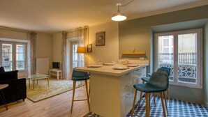 A modern kitchen with a central island, bar stools, and a dining area with a table and chairs. - Appartement T3 de 60 m2 - Centre Historique (Sarlat-la-Canéda)