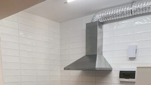 Eine kleine Küche mit weißen Fliesen, einem Edelstahl-Spülbecken, einem schwarzen Backofen und einer integrierten Dunstabzugshaube.