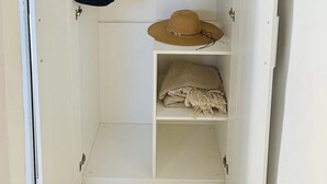 Ein weißer Kleiderschrank mit Kleiderstange links und einem Einlegebrett mit Hut und gefalteter Kleidung rechts.