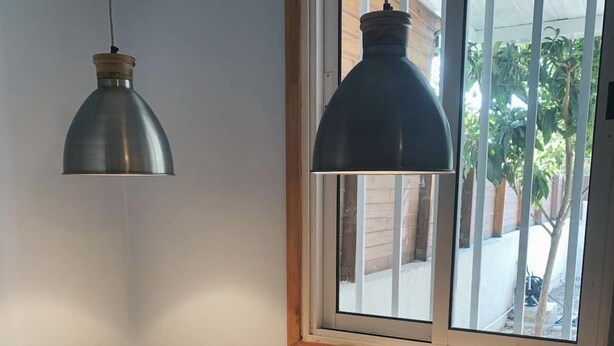 Ein kleiner, moderner Raum mit einem Holztisch, zwei weißen Stühlen, einem Fenster mit Blick auf Grünflächen und zwei Pendelleuchten.