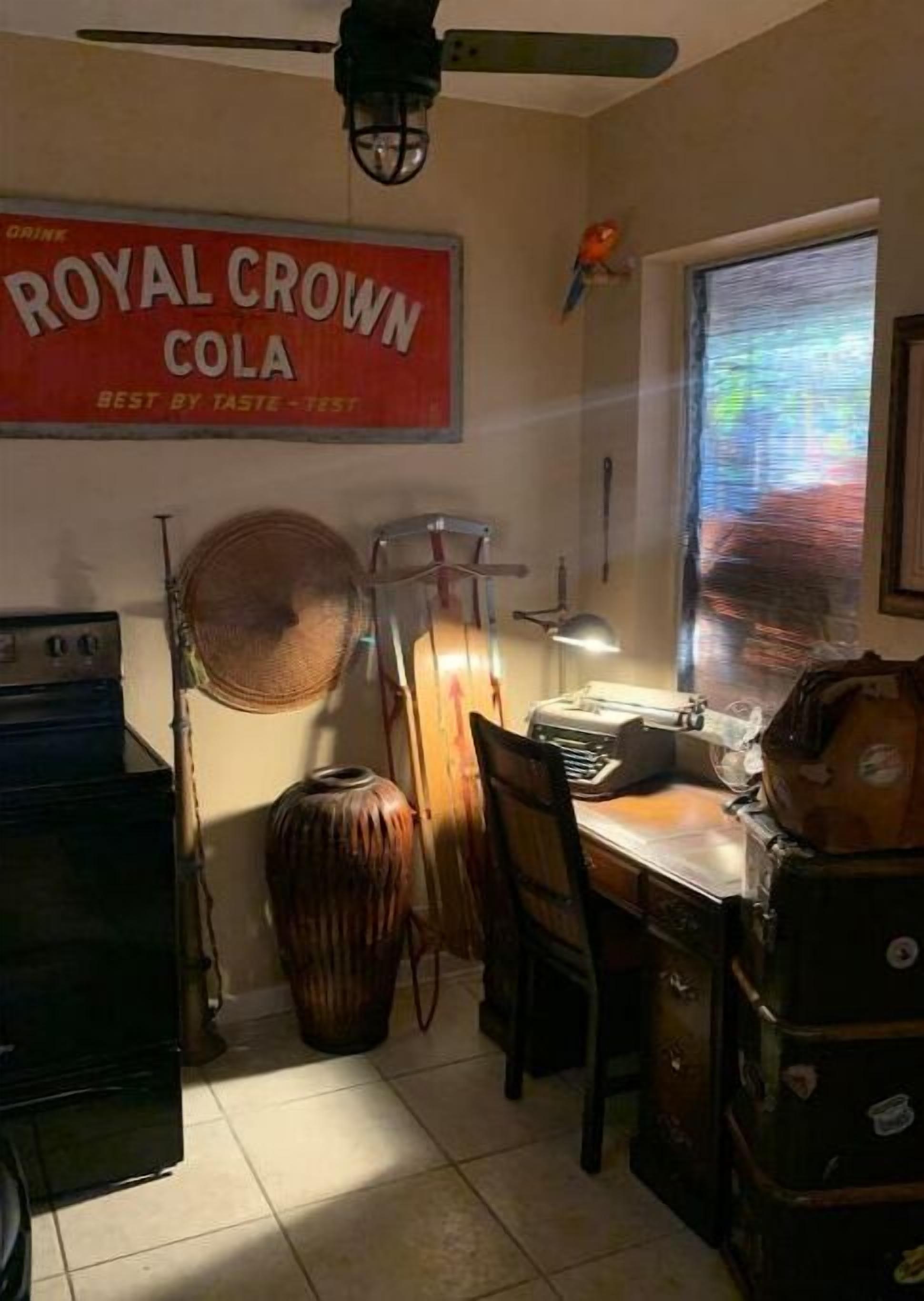 Eine Küche mit einem alten Radio, einem Ventilator, einem Holzstuhl und einem großen Poster von Royal Crown Cola.