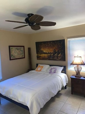 A bedroom with a bed, a ceiling fan, a painting, a lamp, and a window with blinds. - Captin' Joe's Tropical Palm Beach Hot Tub Hideaway (West Palm Beach)