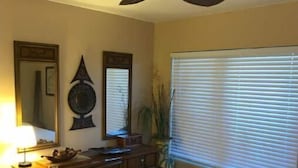 A bedroom with a bed, a ceiling fan, a dresser, a lamp, and a window with blinds.