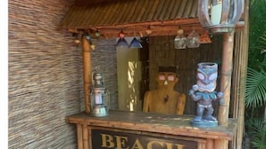 A tiki bar with a sign reading "TIKI BAR" and "BEACH" indicating its location. There are two stools in front of the bar.