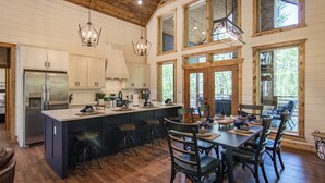 Une cuisine spacieuse dotée d’un grand îlot central, d’un plafond en bois et de grandes fenêtres.