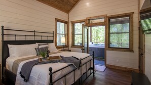Une chambre à coucher avec un grand lit, une table de chevet avec une lampe et une vue sur l’extérieur par une porte.