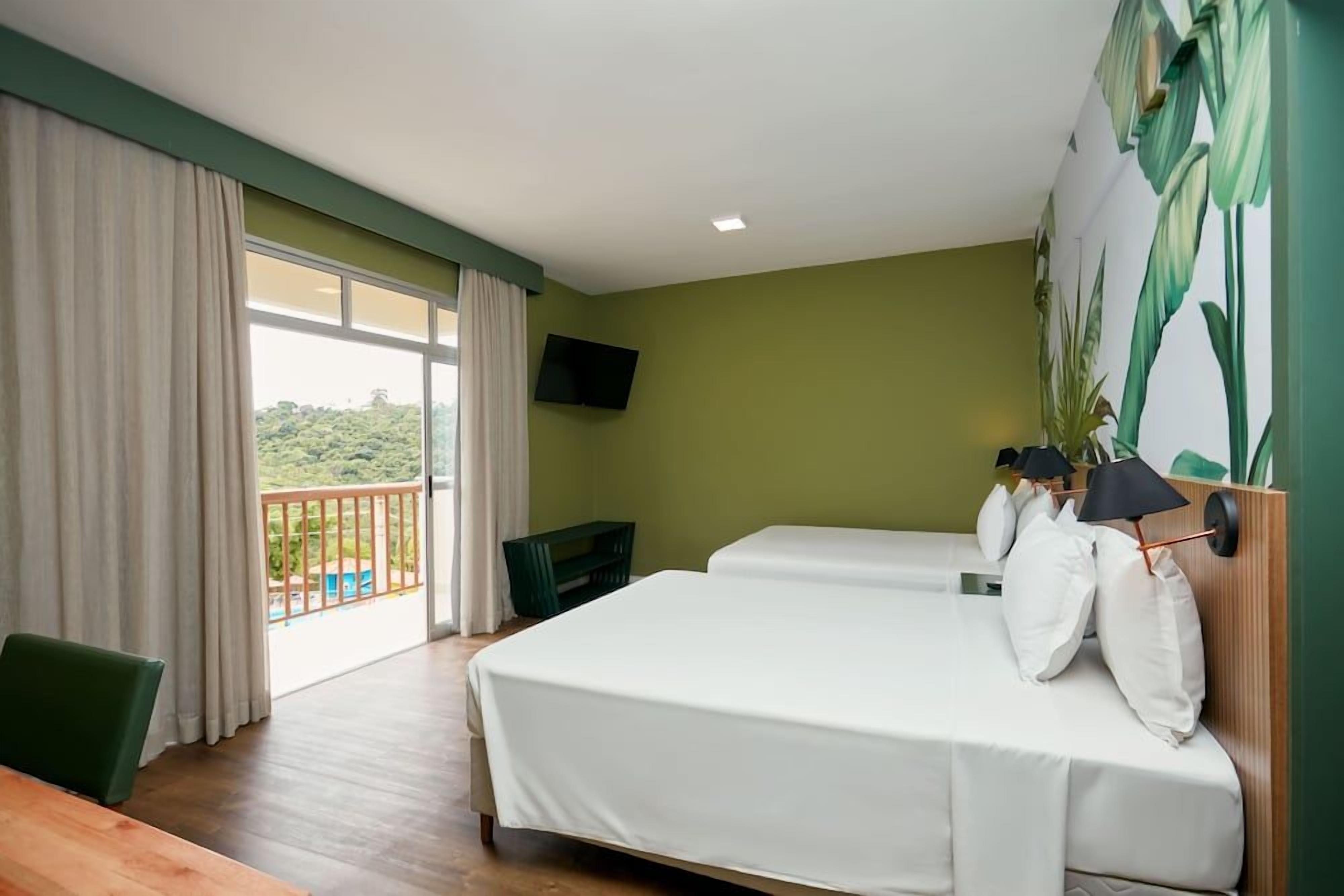 Habitación de hotel con dos camas, balcón, televisión y vistas a zonas verdes.