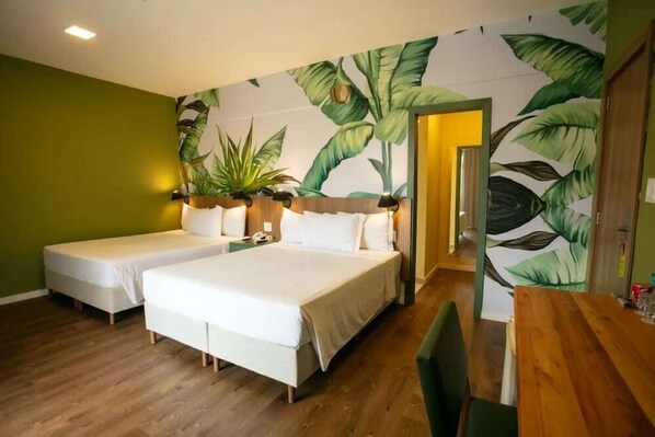 Une chambre d’hôtel avec deux lits, une table à manger en bois et un mur vert orné d’une fresque représentant des feuilles tropicales.