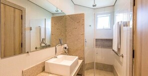 A modern bathroom with a large sink, a mirror, and a shower area.