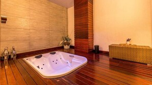 A modern bathroom with a wooden floor, a large bathtub, a wooden column, and a small table with a vase. - Taua Resort & Convention Caete (Caete)