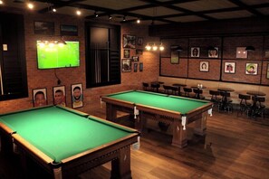 Une salle de billard équipée de deux tables de billard, d’un téléviseur et de tableaux encadrés aux murs.