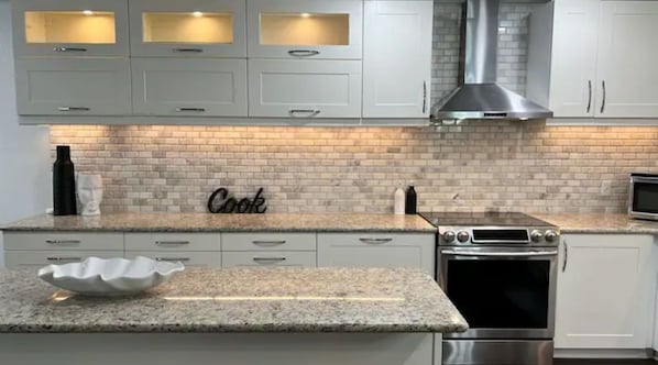 Enjoy cooking in this well-equipped kitchen with a granite countertop, stainless steel appliances, and a brick backsplash.