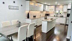 Una cocina moderna con armarios blancos, una isla central y un comedor con una mesa y sillas de madera.