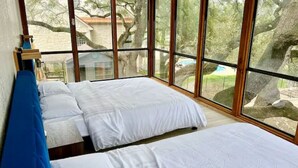 Una habitación con dos camas, ventanas amplias y vistas a árboles y un edificio.