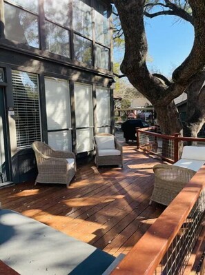 Relax on the deck with wicker chairs and a cushioned bench, surrounded by a tree providing shade.