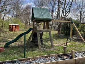 Children can play in the enclosed outdoor area with a wooden playhouse, slide, and swing set.