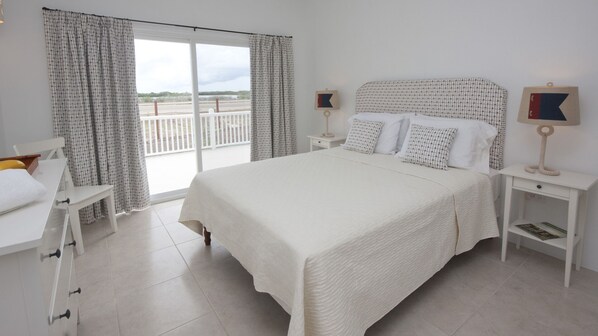 A spacious bedroom with a large bed, white walls, and a balcony with curtains. - Close to beach. Peaceful location. Private pool. (St Mary's)