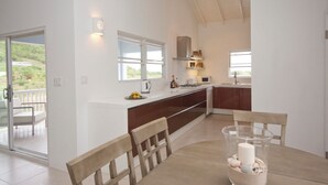 A modern kitchen with a large island, a dining area with a glass table, and a balcony with outdoor seating. - Close to beach. Peaceful location. Private pool. (St Mary's)
