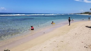 Een strand met helderblauw water, mensen die zwemmen en ontspannen, en een zandstrand.