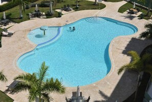 Une grande piscine de forme irrégulière, entourée d’une terrasse sablonneuse, agrémentée de chaises longues et de palmiers.