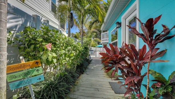 Een houten pad dat leidt naar een turquoise gebouw met een bord waarop de richting naar Sunshine, Starfish en Seashell staat aangegeven.