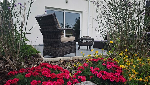 A garden with red and yellow flowers, a wicker chair, and a stone bench. - Traditional Connemara Retreat | 5 Mins to Aran Ferry (Co. na Gaillimhe)