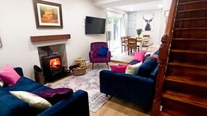 A living room with a fireplace, a sofa, a chair, and a dining area with a table and chairs. - Traditional Connemara Retreat | 5 Mins to Aran Ferry (Co. na Gaillimhe)