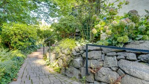 A stone wall with a metal railing, a paved pathway, and lush greenery. - 1 Mi to Park & Waterfront! Seattle Home w/ Balcony (Seattle)