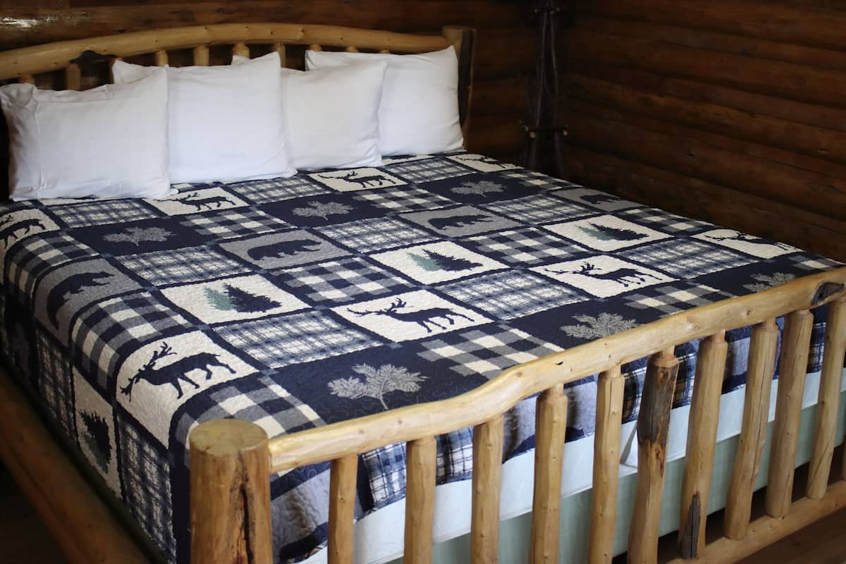 Un lit en bois avec une courtepointe à carreaux ornée de motifs représentant des animaux et des feuilles.