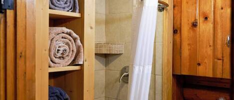 A wooden bathroom with a shower, a toilet, and shelves with towels.