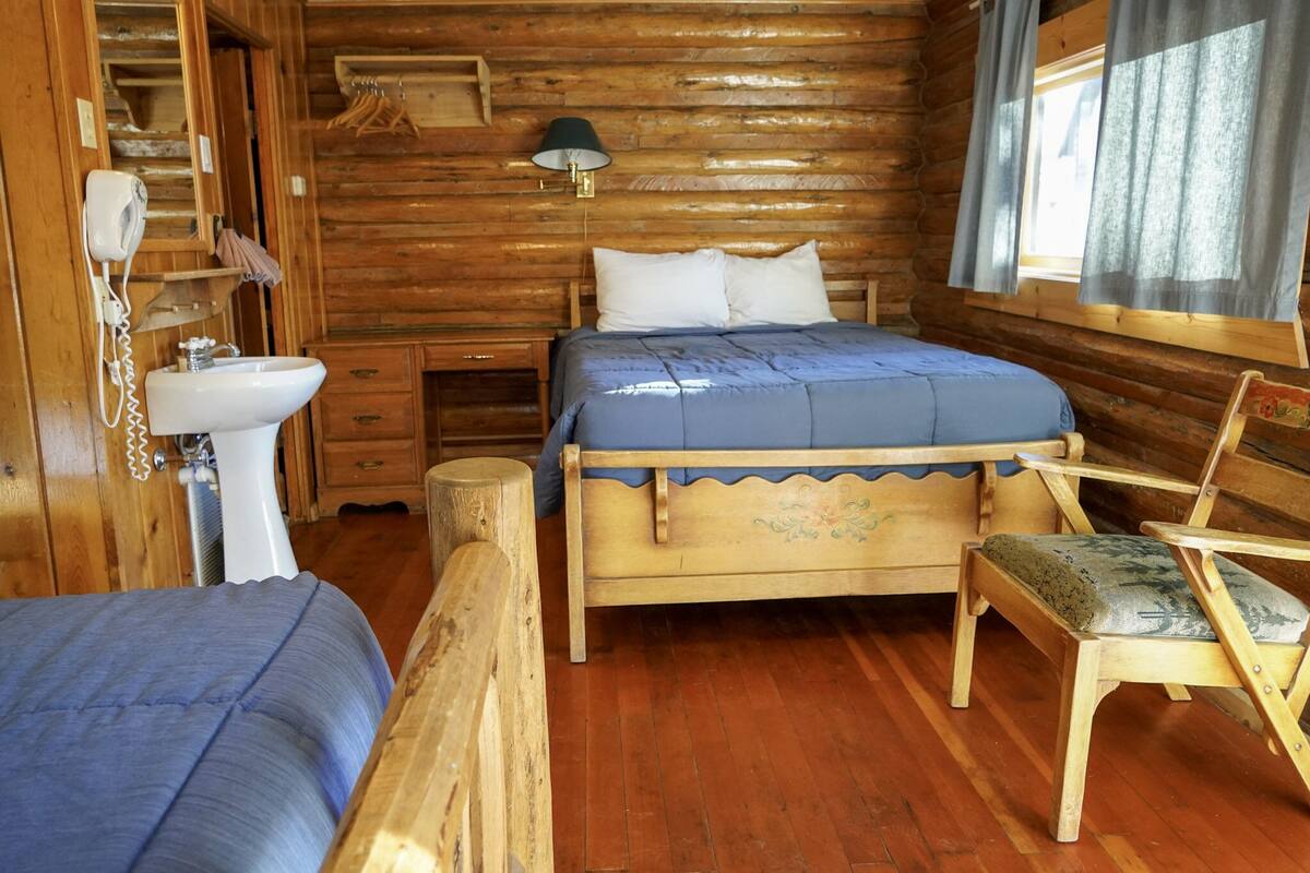 Une pièce de cabane en bois comprenant un lit, une chaise, un lavabo et une lampe.