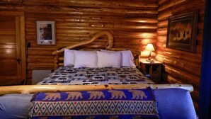 Una habitación tipo cabaña de madera con una cama, una mesita de noche y un cuadro colgado en la pared.