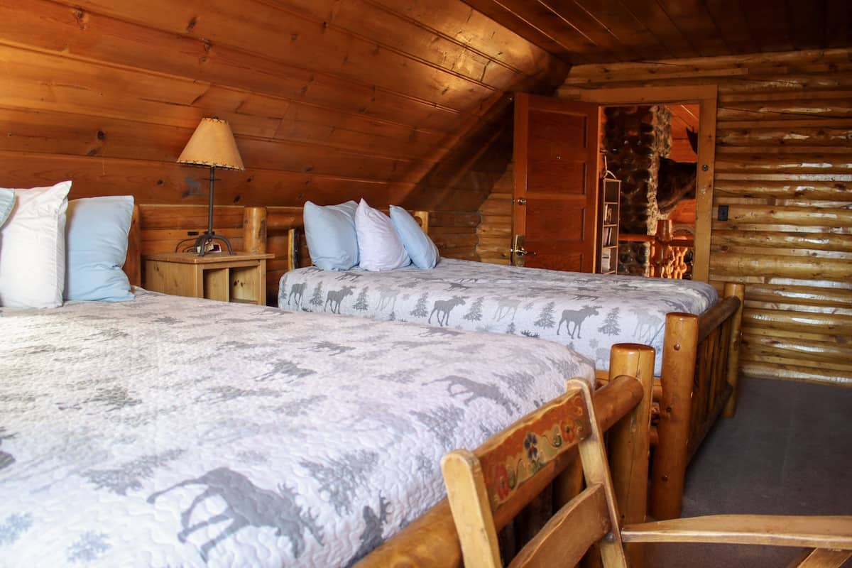 Une chambre confortable dans un chalet en rondins, avec deux lits, une tête de lit en bois et une table de chevet avec une lampe.