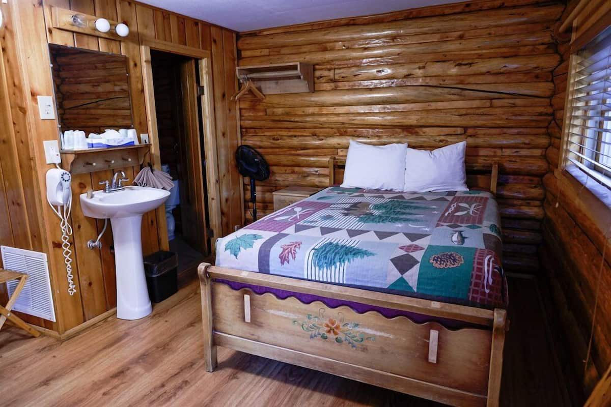 Une chambre dans une cabane en bois, avec un lit, une table de chevet, une lampe suspendue et une porte en bois.