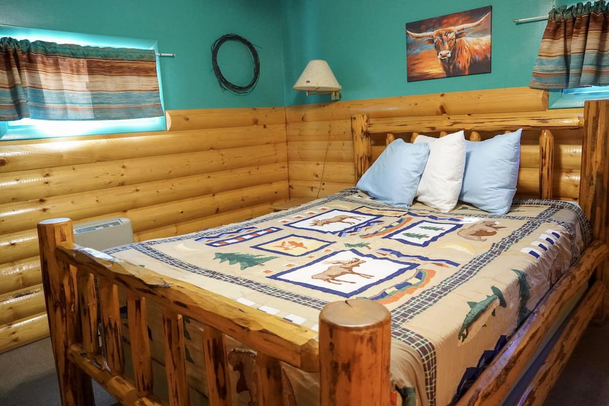 Une pièce rustique aménagée dans un chalet en rondins, avec un lit, une table et une lampe.