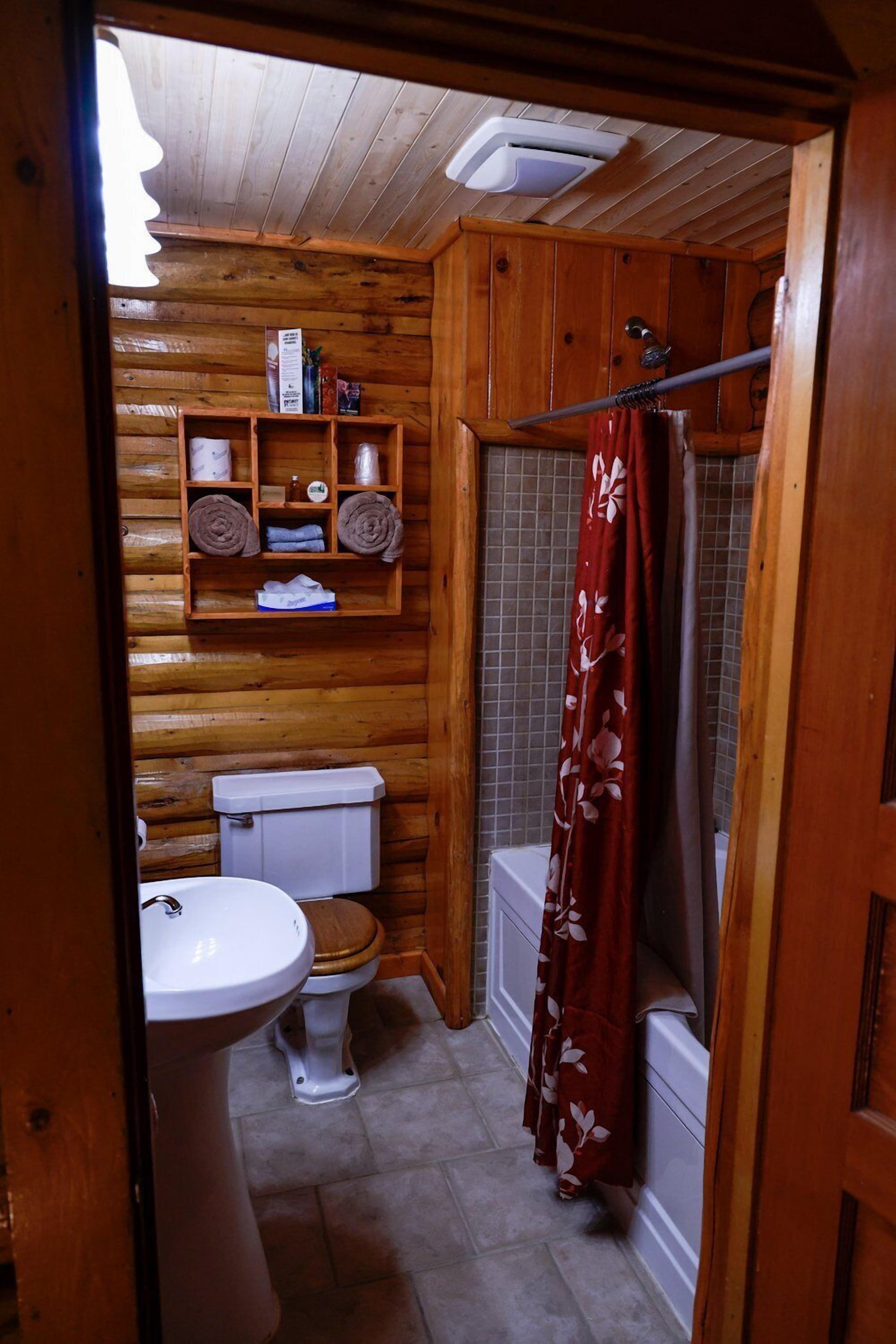 Une salle de bain rustique, aménagée dans une cabane en bois, avec des toilettes, un lavabo et une douche.