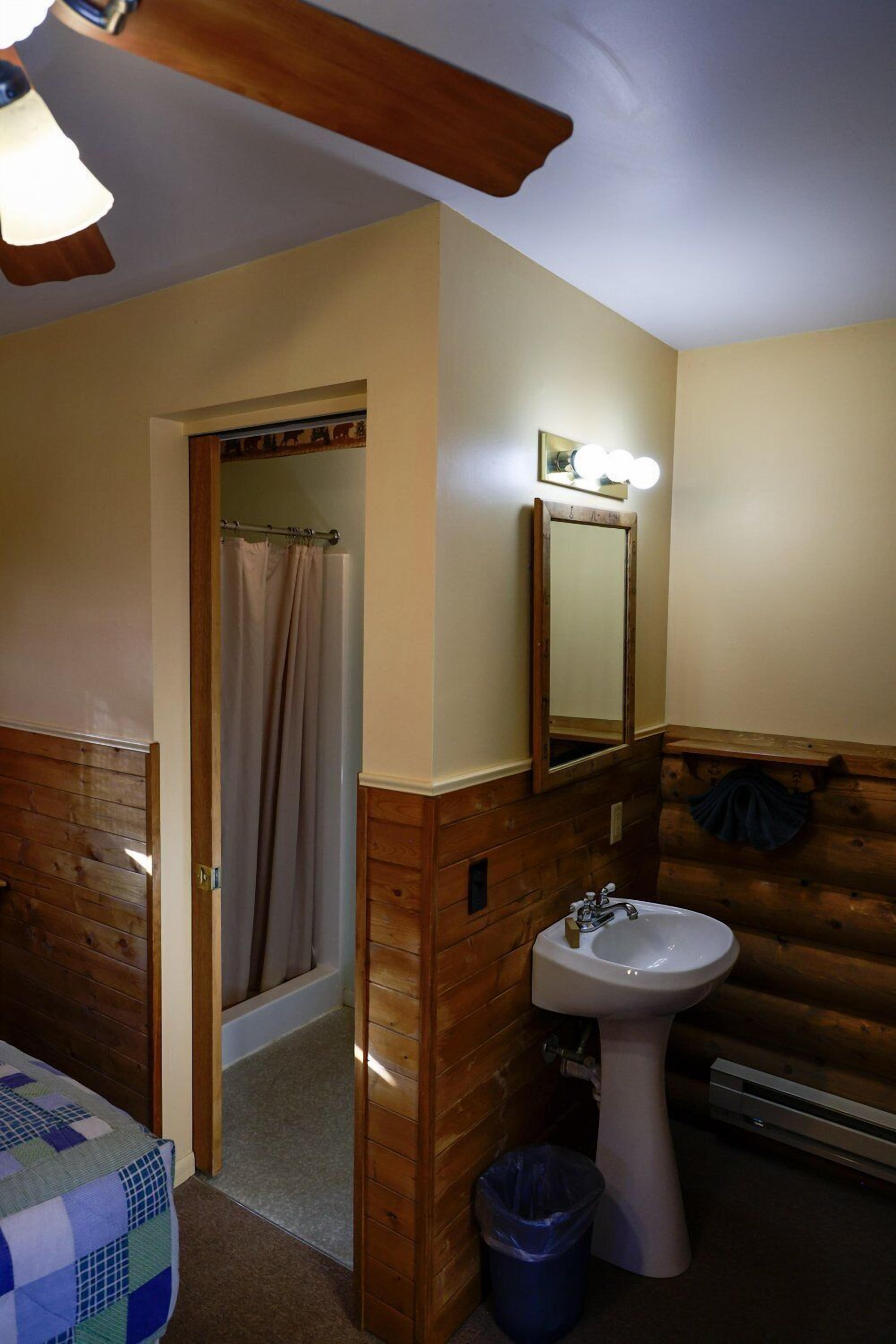 A bathroom with a wooden wall, a sink, a mirror with lights, and a ceiling fan.