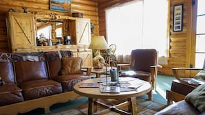 Un interior de cabaña acogedor, con un sofá de cuero, una mesa redonda de madera y decoración rústica.