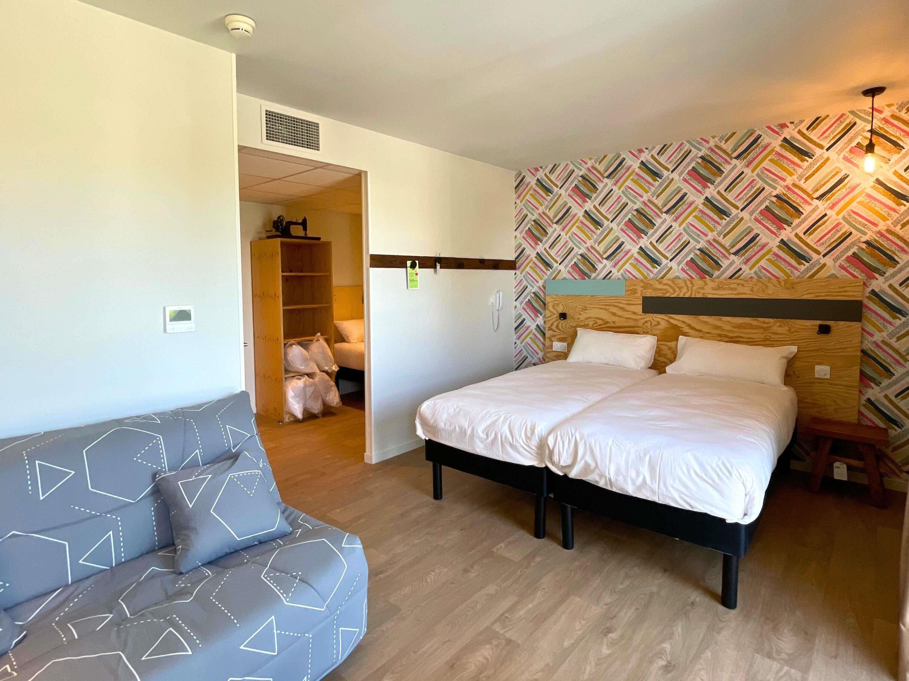 A bedroom with a bed, a sofa, a wooden headboard, and a patterned wall.