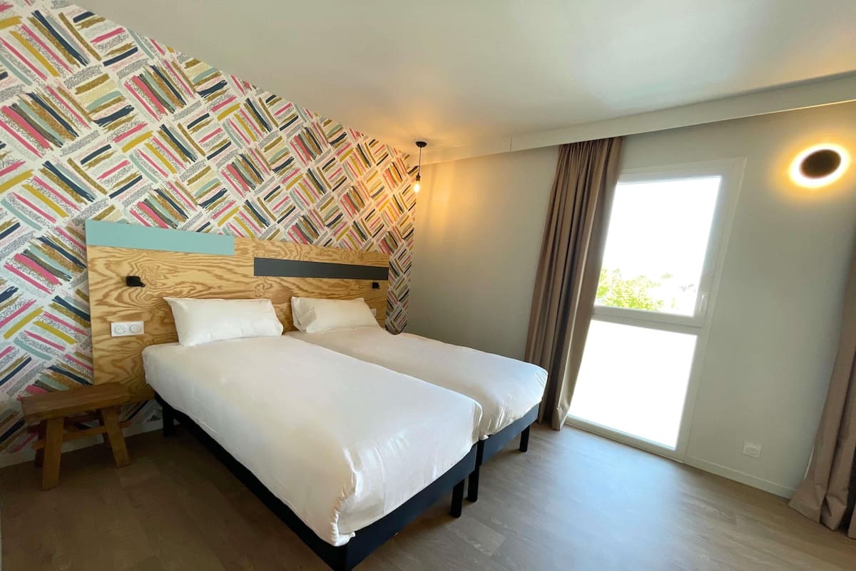 A double bed with a wooden headboard, a nightstand, and a patterned wall.