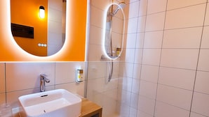 A modern bathroom with a white sink, a mirror with an oval frame, and a shower area with a handheld showerhead. - greet hotel Castets Coeur des Landes (Castets)