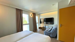 Une chambre d’hôtel dotée d’un grand lit, d’un coin salon avec un canapé, d’un téléviseur à écran plat fixé au mur et d’une porte.
