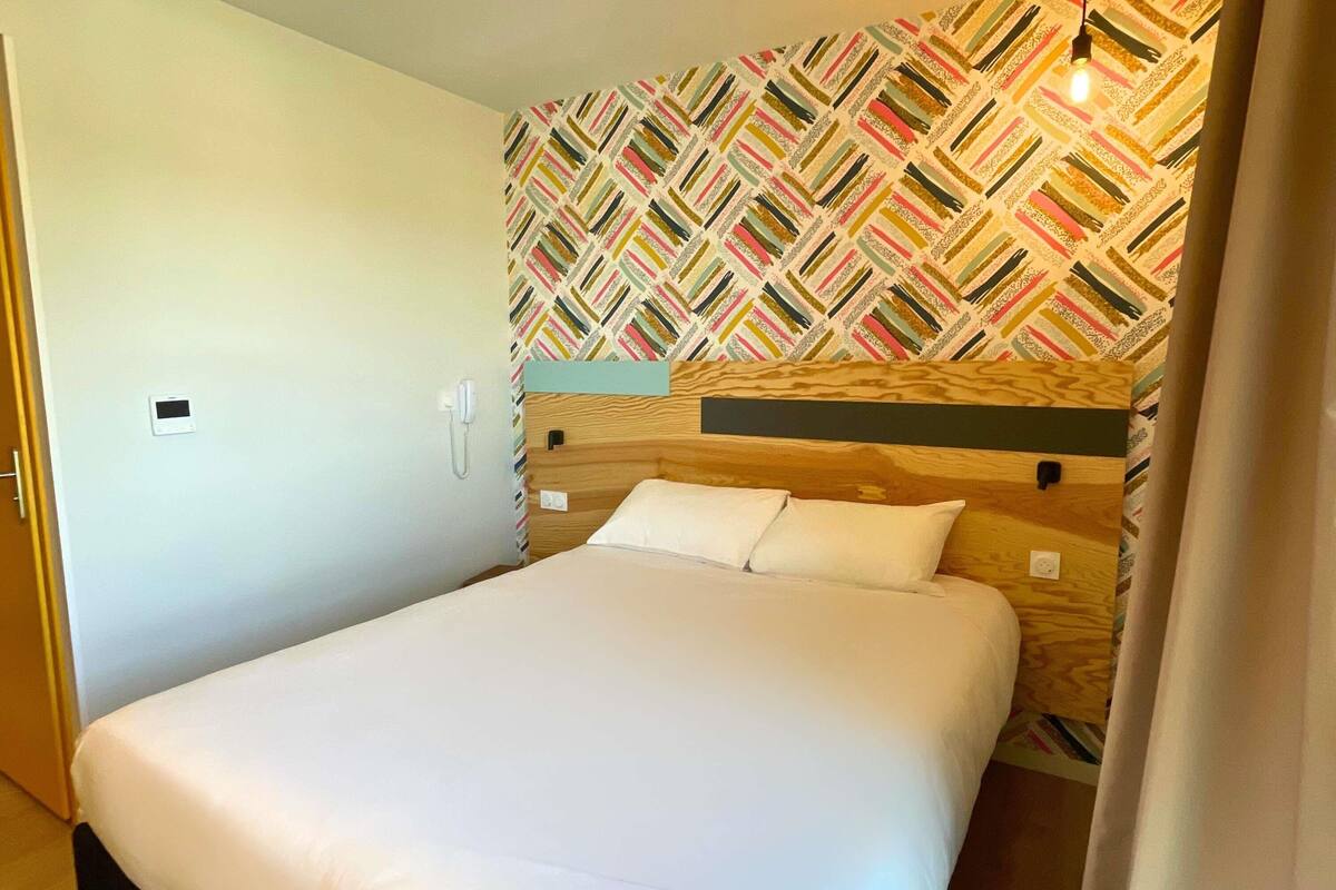 A neatly made bed in a room with a patterned wallpaper and a wooden headboard.
