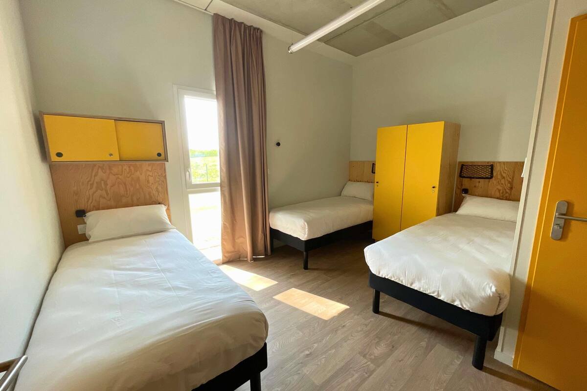 A room with two beds, a wooden wardrobe, a door, and a window with curtains.