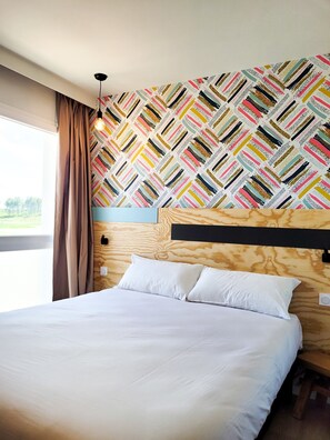 A bedroom with a patterned wallpaper, a wooden headboard, and a large bed with white linens.